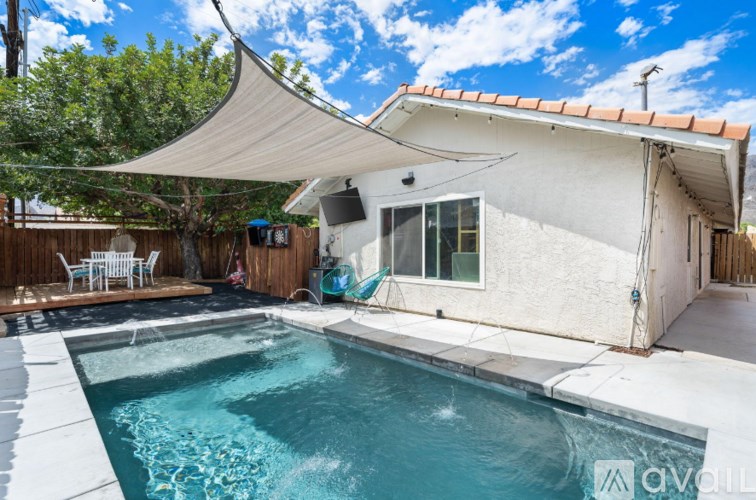 A pool in a backyard with a patio and a white shade sail.