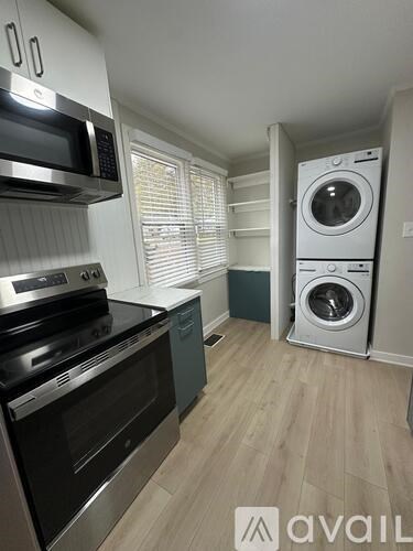 A kitchen with a stove top oven, microwave, and a washer and dryer in the corner.