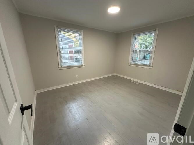 A room with a light grey floor and two windows with white blinds.