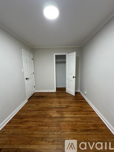 A room with wooden floors and white walls, with a door on the left and an open doorway on the right.