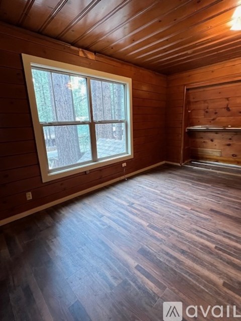 A room with wooden walls and floors has a window and a wooden shelf.
