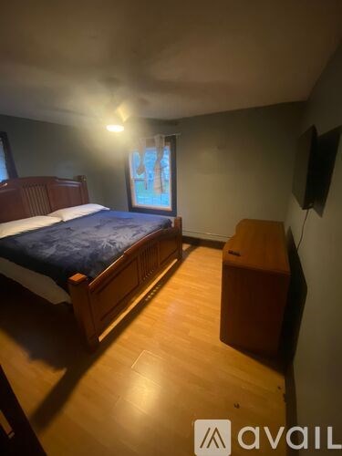 A bedroom with a bed, wooden dresser, and a window with a view of a body of water.