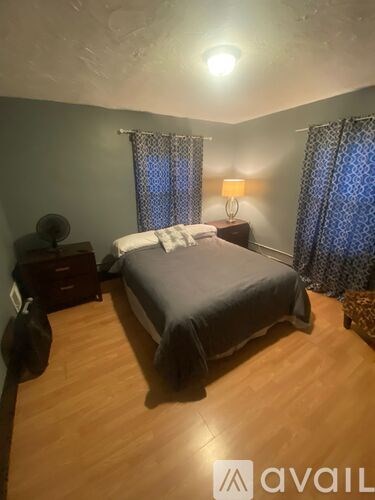 A bedroom with a bed, nightstand, and window with curtains.