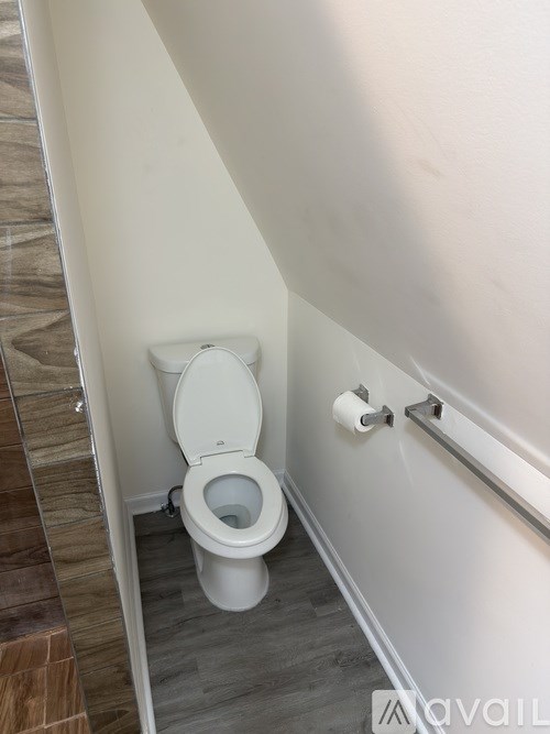 A white toilet in a small bathroom with wood flooring.