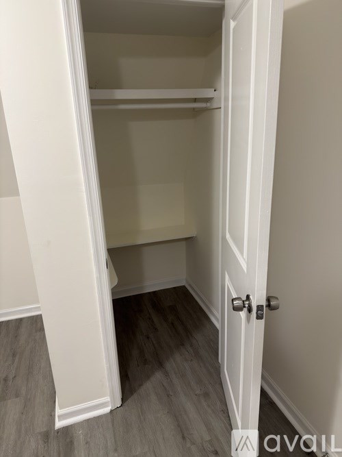 A white door with a handle is open to a room with a white wall and a wooden floor.