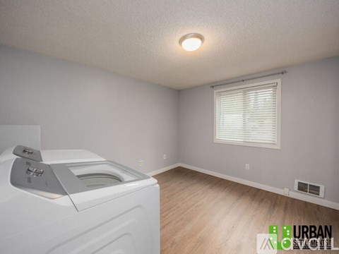 A white washing machine sits in a room with a window and a wooden floor.