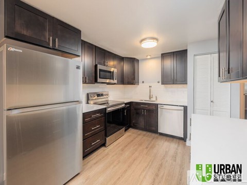 A modern kitchen with a stainless steel refrigerator and wooden flooring.