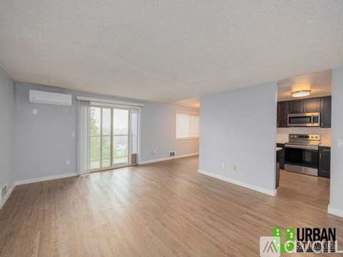 A spacious living room with wooden flooring and a kitchen area in the background.