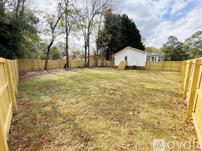 A backyard with a white house, a wooden fence, and trees.