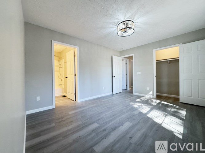 A spacious room with wooden flooring and white walls, with a light fixture on the ceiling and a doorway leading to another room.