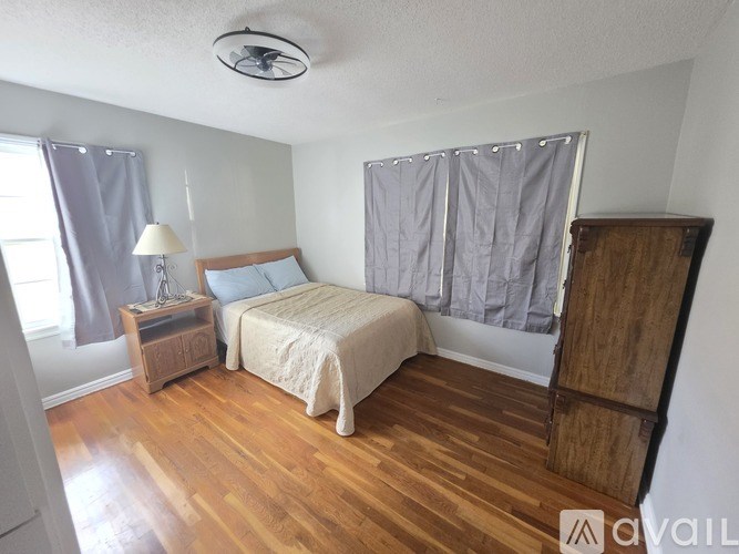 A bedroom with a bed, nightstand, and wooden floor.