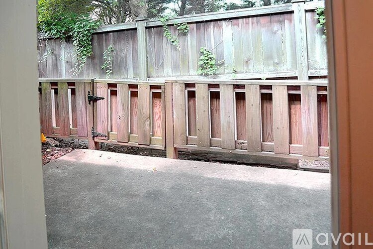 A wooden fence with a gate is in front of a green hedge.