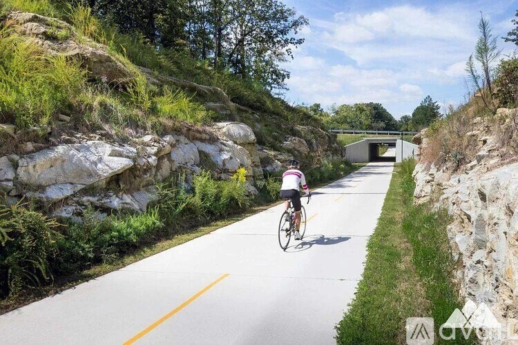 A cyclist is riding down a paved road with a stone wall on one side and a tunnel entrance on the other.