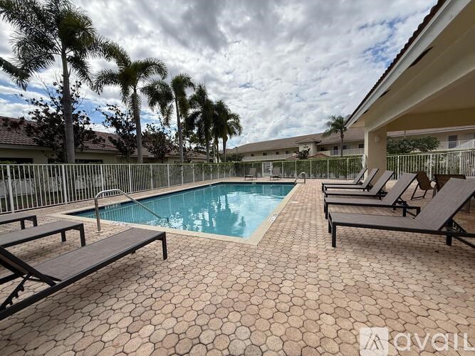 A pool surrounded by lounge chairs and palm trees.
