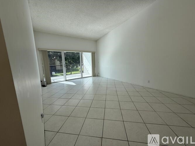 A spacious room with white tiled flooring and a sliding glass door leading to a balcony.