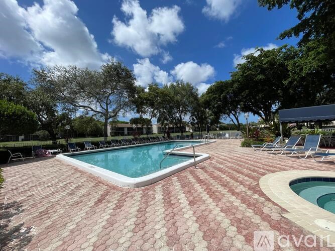 A large outdoor swimming pool surrounded by a brick patio and lounge chairs.