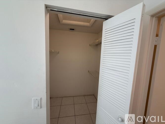 A white door is open to a small, empty room with a tiled floor and a ceiling fan.