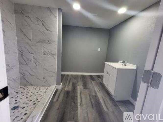 A bathroom with a marble wall and wooden floor.
