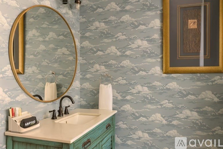 A bathroom with a blue patterned wallpaper and a round mirror above a sink.
