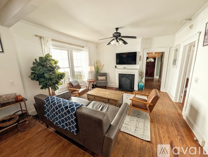 A living room with a couch, a chair, a table, a television, a plant, and a fireplace.