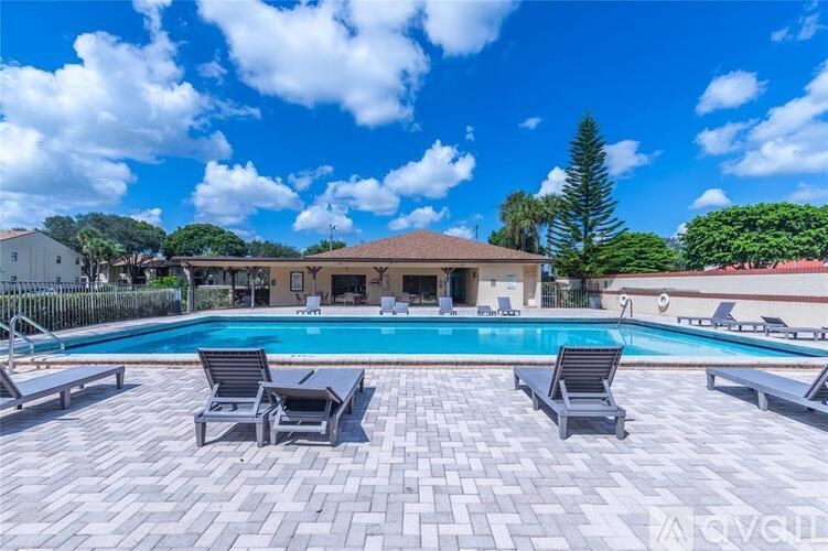 A swimming pool surrounded by a patio with chairs and a house in the background.