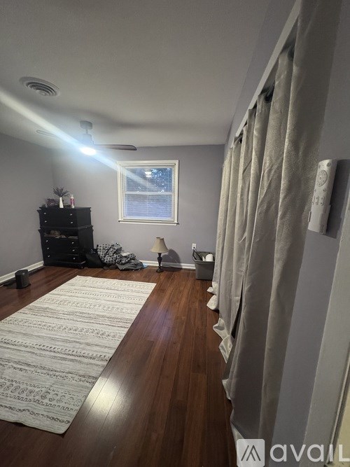 A room with a rug on the floor and a window with curtains.