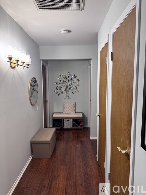 A hallway with a wooden floor, a white bench, and a wall-mounted light fixture.