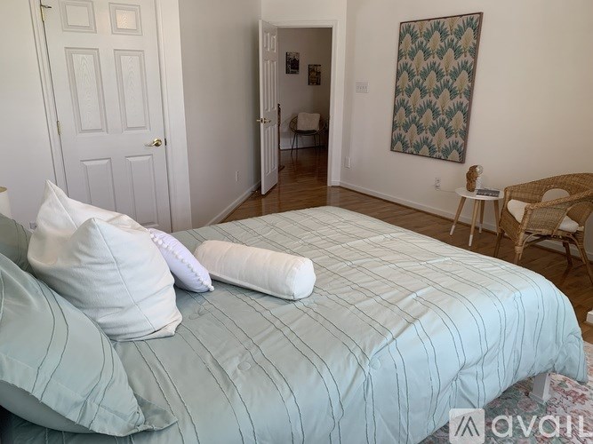 A bed with a striped comforter and two pillows sits in a room with a chair and a patterned wall hanging.