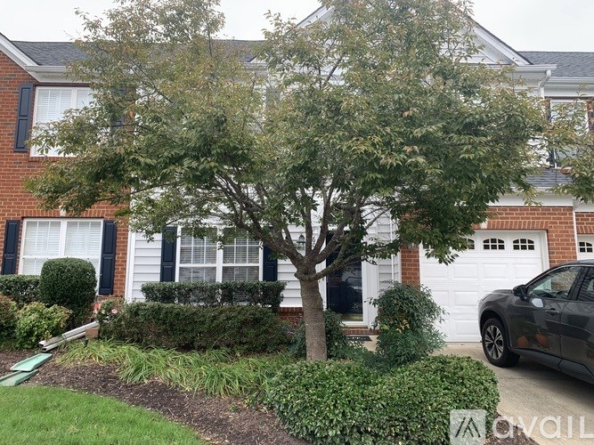 A tree in front of a house with a car parked in the driveway.