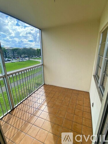A balcony with tiled flooring and a view of a parking lot and trees.