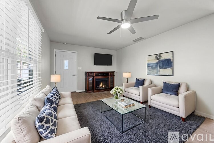 A living room with a white couch, a glass coffee table, and a television mounted on the wall.