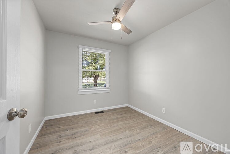 A room with a ceiling fan and a window with a view of trees.