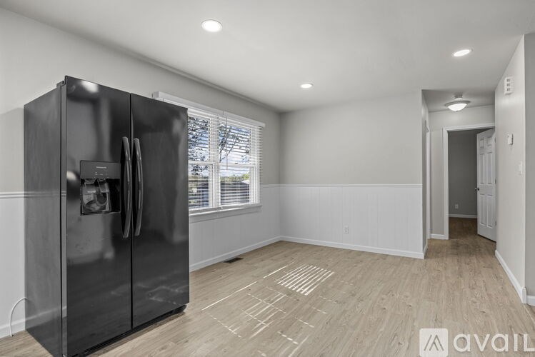 A black refrigerator is in a kitchen with wood flooring and white walls.