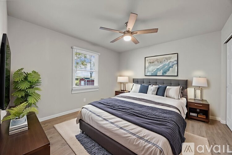 A bedroom with a bed, a ceiling fan, and a painting on the wall.