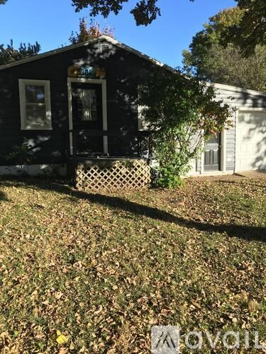 A small house with a porch and a tree in front.