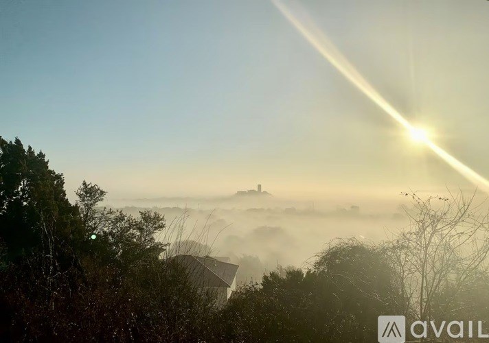A sunrise or sunset scene with a misty landscape and a house in the distance.