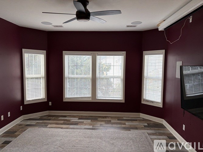 A room with a ceiling fan and three windows.