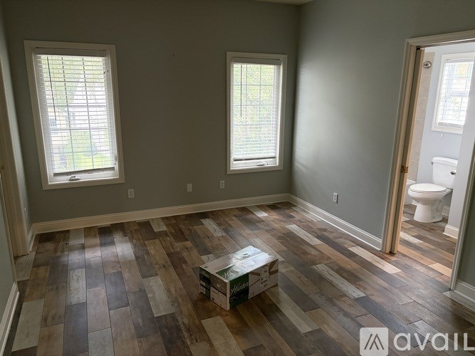 A room with wooden flooring and two windows.