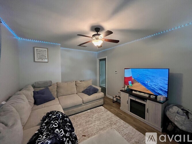 A living room with a beige couch, a flat screen TV, and a ceiling fan.