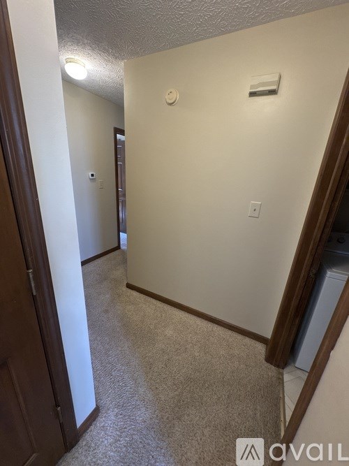 A hallway with a carpeted floor and a light switch on the wall.