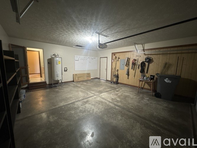 A large, empty room with a concrete floor and walls, equipped with a workbench and various tools hanging on the wall.