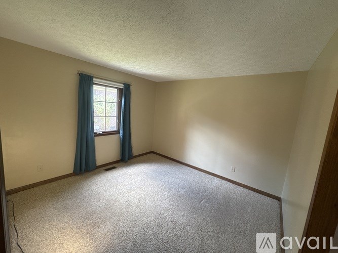 A room with a carpeted floor and a window with blue curtains.