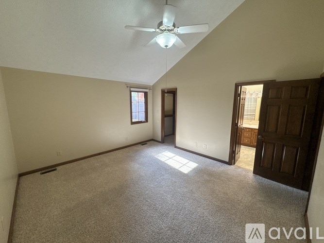 A room with a carpeted floor, a ceiling fan, and a door leading to another room.