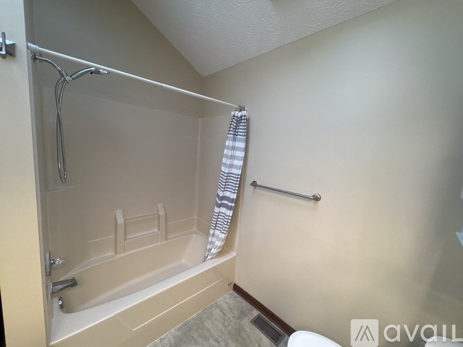 A bathroom with a beige tub and a striped towel hanging on the shower rod.