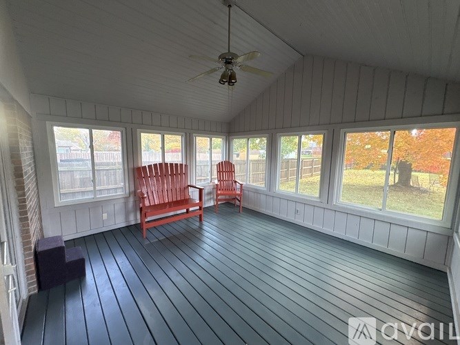 A sunroom with a ceiling fan and three red chairs.