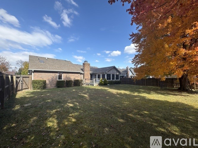 A house with a fenced yard and a tree with orange leaves.