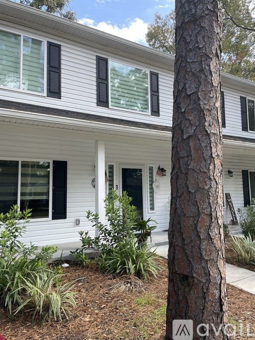 A white house with a black door and a tree in front.