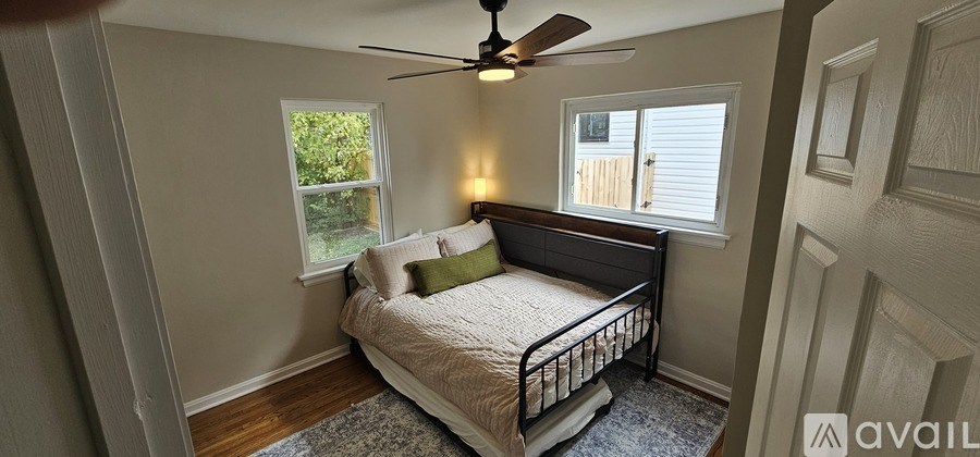 A bedroom with a bed, a ceiling fan, and a window with a view of a fence.