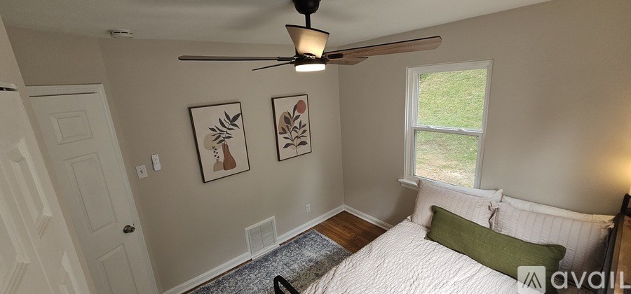 A bedroom with a bed, a ceiling fan, and two framed pictures on the wall.