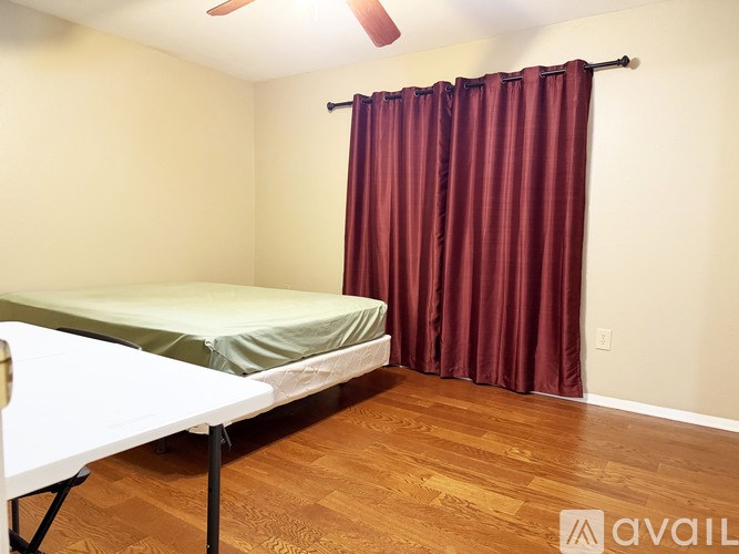 A bedroom with a bed, a table, and a curtain.